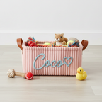 Pink corduroy dog toy basket Coco with toys scattered around